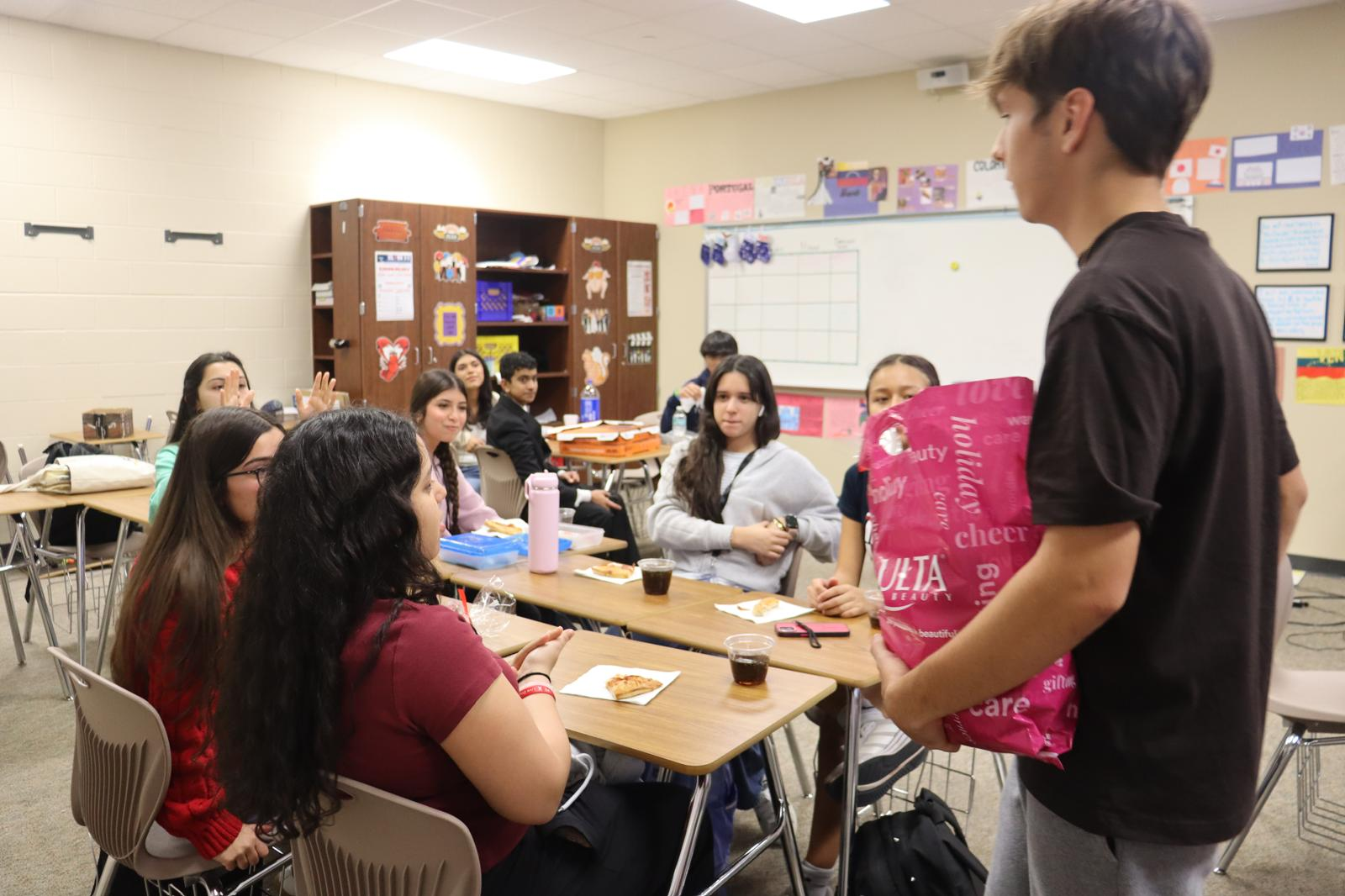 A student speaking to club members seated around desks during a meeting