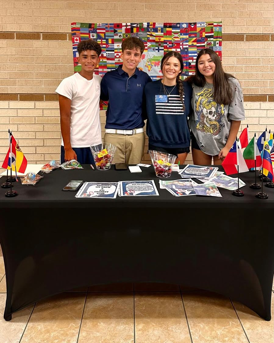 Four club members standing behind the Club Expo table decorated with international flags